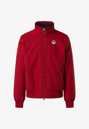 Giacca bomber rossa con colletto alto, chiusura a zip frontale, tasche laterali e polsini a costine. Presenta una patch rotonda blu sul lato sinistro del petto.