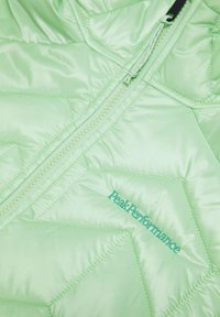 Light green puffer jacket with a quilted texture and a zip closure. Features "PeakPerformance" embroidered in matching green.
