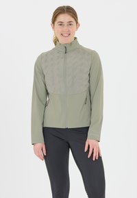 Lättviktsgrön jacka med quiltad framsida, hög krage, dragkedja och sidofickor. Matchad med svarta, åtsittande byxor, minimalistisk design.