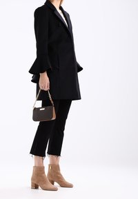 Zwarte jas met uitlopende mouwen, zwarte getailleerde broek, tan suède enkellaarsjes en een kleine twee-kleurige handtas. Eenvoudige en moderne ontwerpelementen.