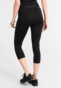 Leggings capri neri con una texture liscia e una cintura ampia. Presentano un design aderente e una lunghezza accorciata, abbinati a scarpe da ginnastica nere.