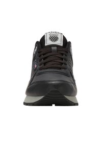 Pohled zepředu na černou sneaker K-Swiss s tkaničkami, síťovaným jazykem, logem na jazyku a bílou podešví s černým vzorkem.