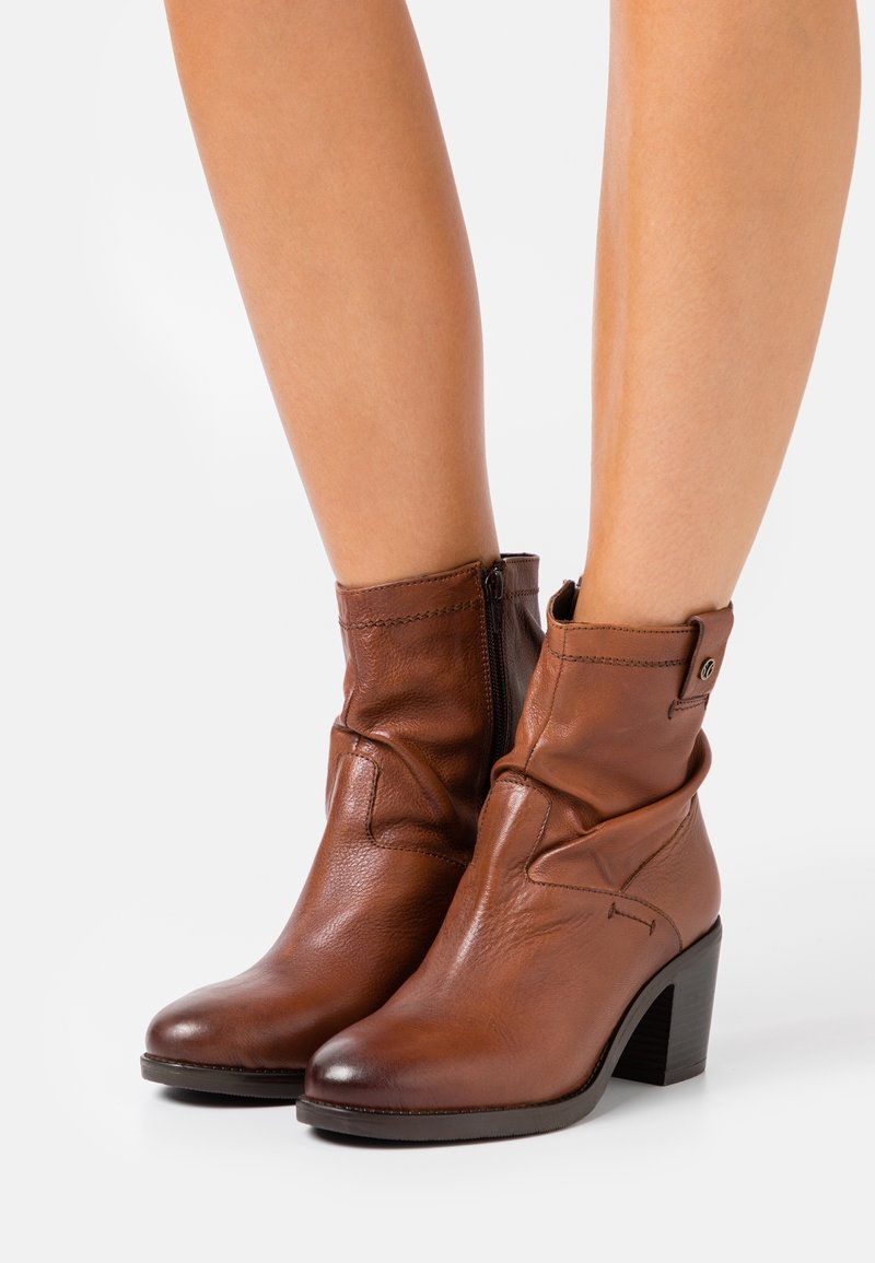 Bottines en cuir marron avec une texture lisse, fermeture éclair et un talon bloc solide. Présente des bords roulés et un détail de couture subtil.