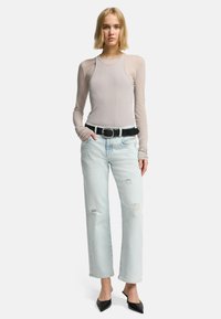 Maglia grigia chiara a maniche lunghe con texture a coste, abbinata a jeans azzurri strappati e una cintura nera. Scarpe nere a punta completano l'outfit.