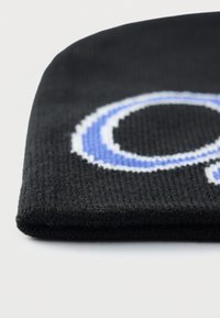 Căciulă tricotată neagră cu un logo mare albastru și alb, cu material texturat și tiv pliat.