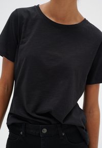 Tricou din bumbac negru, cu guler rotund și mâneci scurte, având o croială lejeră și o textură fină. Asortat cu pantaloni negri.