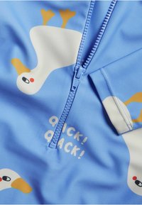 Blauer Badeanzug mit Reißverschluss, dekoriert mit weißen Enten, gelben Akzenten und dem Text "QUICK! QUACK!" in Weiß. Weiches, dehnbares Material.
