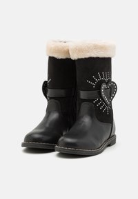 Bottes en suède noir avec un revers en fausse fourrure, ornées d'un accent en forme de cœur et de clous décoratifs en argent, dotées d'une semelle plate et d'une fermeture éclair.