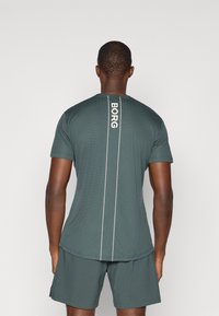 Roheline sportlik T-särk lühikeste varrukatega, tekstuurse kangaga ja vertikaalse valge "BORG" logo ning valgete detailidega seljal.