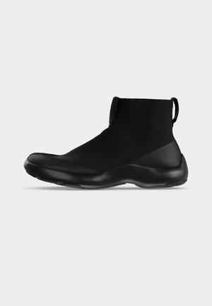 Zwarte hoge sneaker met rekbare stoffen bovenkant, treklus op de hiel en een dikke, gevoerde zool.