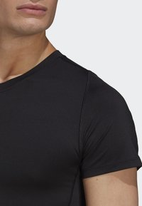 Camiseta deportiva negra con una textura suave y lisa, mangas cortas y un cuello redondo con detalles de costura visibles.