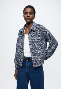 Ζακέτα με μοτίβο ζέβρας σε μπλε και κρεμ, με γιακά, κουμπιά μπροστά και ελαστικές μανσέτες. Συνδυάζεται με ψηλόμεσο τζιν παντελόνι.