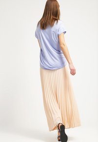 Svetle modrá košile s krátkým rukávem spárovaná s plynulou, plisovanou broskvovou maxi sukni. Sukně má texturovaný design a sahá až k kotníkům.