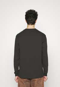 Black long-sleeve shirt made of cotton, featuring a crew neck and cuffs, worn with patterned brown pants, shown from the back.