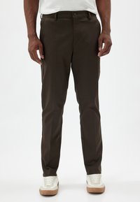 Pantalon marron foncé avec une texture lisse, coupe ajustée et poches avant, associé à des baskets blanches avec des accents beiges.