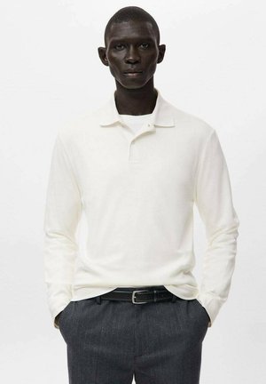 Polo de manga larga en color blanco roto, confeccionado con tela suave, con cuello puntiagudo y ajuste entallado, combinado con pantalones oscuros de raya diplomática.