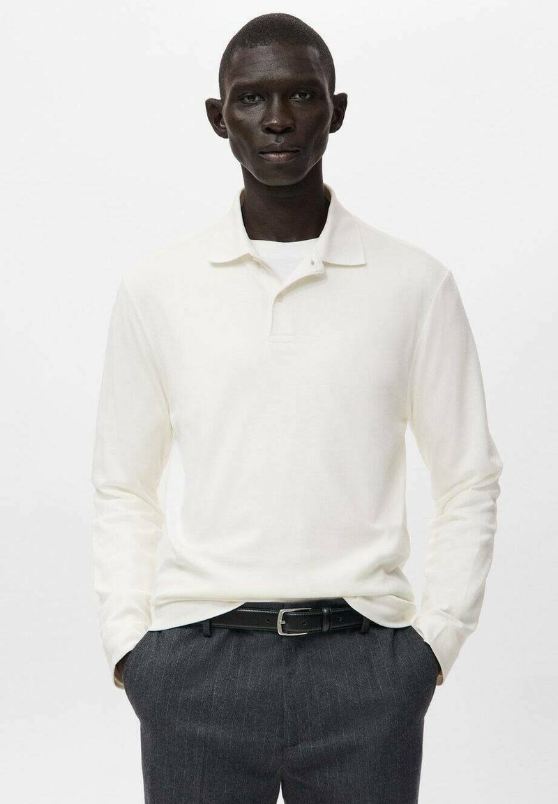 Langärmliges Poloshirt in Off-White, aus weichem Stoff, mit spitzem Kragen und schmaler Passform, kombiniert mit dunklen Nadelstreifenhosen.