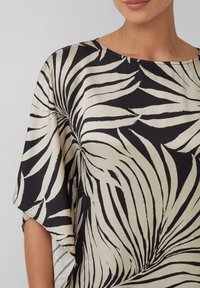 Zwart en crèmekleurige blouse met een palmbladerenprint, zachte textuur, ronde halslijn en losse mouwen. Ontwerp benadrukt gedurfde, contrasterende patronen.