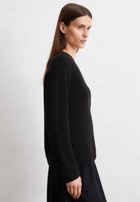 Schwarzer Strickpullover mit strukturiertem Muster, ausgestattet mit V-Ausschnitt und langen Ärmeln, seitlich gegen einen neutralen Hintergrund präsentiert.