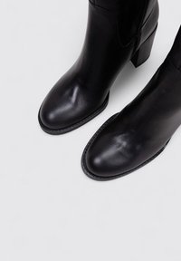 Botines de cuero negro con un diseño elegante, punta redonda y tacón cuadrado. Presentan una textura suave y costuras visibles a lo largo de la suela.
