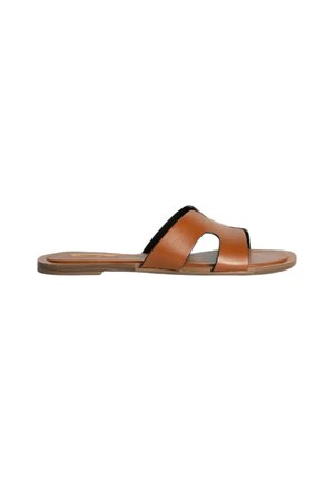 Sandal de piel marrón con una cinta ancha y curva y un detalle cortado. Suela plana con una base color tostado y un diseño minimalista.