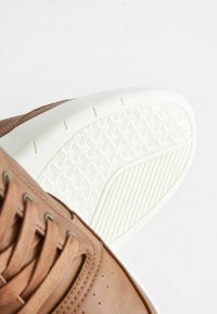 Bruna lädersneakers med snörning, vit gummikärna med texturerat mönster. Innehåller perforerade detaljer på sidorna.