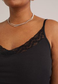 Frau trägt ein schwarzes Hemdchen mit Spitzenbesatz und eine silberne Doppelkettenhalskette, die Nacken, Schlüsselbein und oberen Brustbereich zeigt.