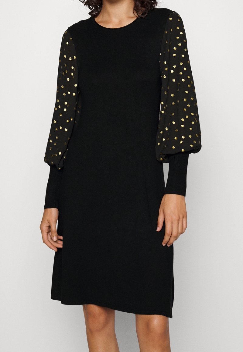 Svart klänning med långa, puffiga ärmar som har guldprickar. Tillverkad av mjukt tyg med rund halsringning och en avslappnad passform.