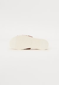 Brune sandaler med en teksturert stropp, kremfarget gummisåle og ribbet mønster for grep. Har en logo på sålen.