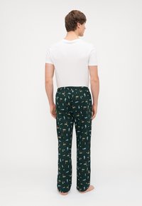 Pantaloni de pijama verzi cu un tiv ajustabil, având un imprimeu repetat de cocktailuri și tee-uri de golf. Material moale cu o croială lejeră.