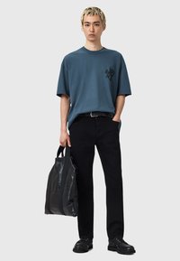 Camiseta de algodón azul de gran tamaño con detalles gráficos en negro, pantalones negros y bolsa de cuero negro, con dos asas y una textura suave.