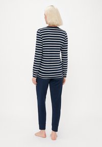 Marineblauw en witte gestreepte top met lange mouwen, gecombineerd met effen marineblauwe joggingbroek. Zachte textuur, casual fit, enkelsluiting op de broek.