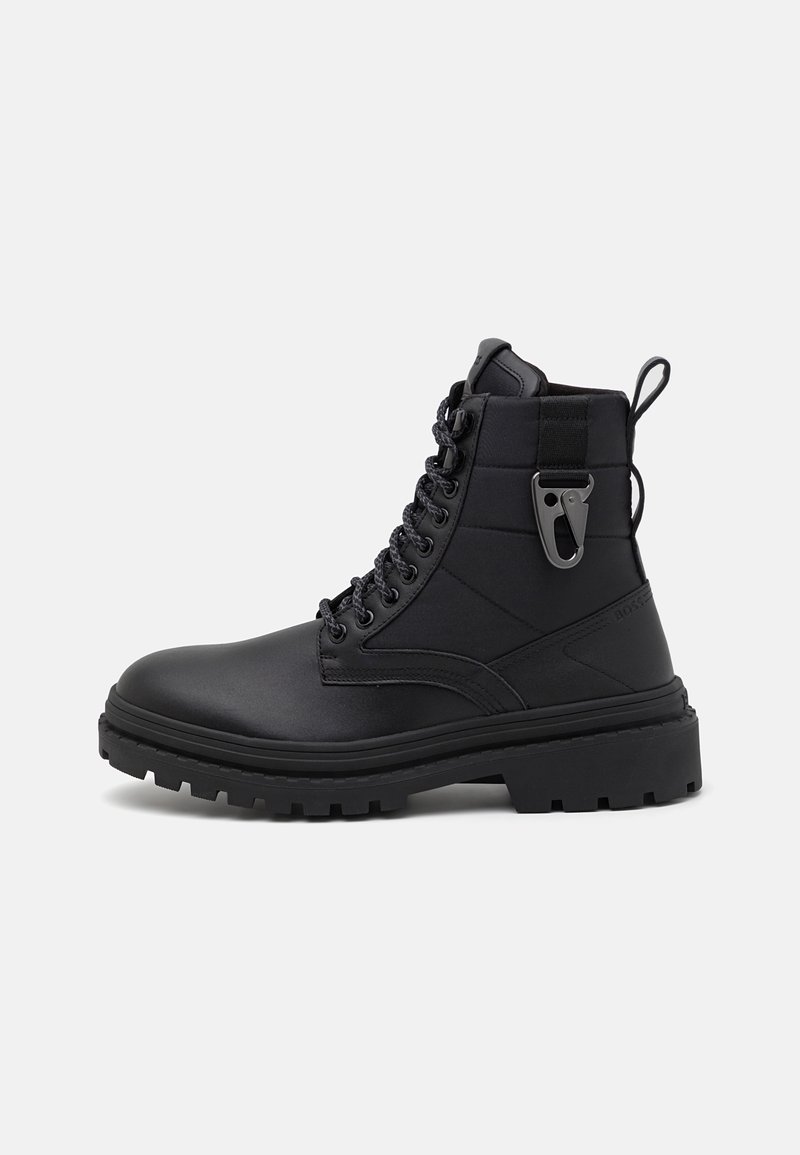 Botte de combat noire à lacets, semelle à épais crampons, cheville rembourrée et détail mousqueton métallique sur le côté extérieur.