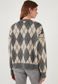 Volneno pulover z diamantskim vzorcem v sivi, kremni in rjavi barvi. Oblikovanje vključuje rebrast rob in manšete ter udoben kroj.