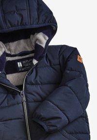 Navy puffer jacket with a zip closure, hood, and striped fleece lining. Features elasticized cuffs and a tan leather tag on the shoulder.