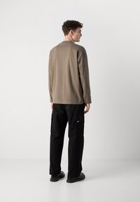 Chemise à manches longues vert olive associée à un pantalon cargo noir. La chemise a une coupe décontractée ; le pantalon présente des poches latérales et une coupe droite.