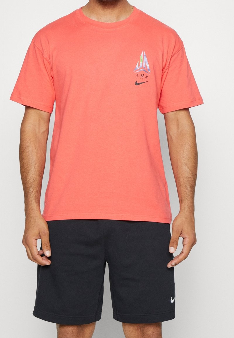 Coral cotton t-shirt with a crew neck, short sleeves, and a printed triangular design on the left chest featuring the Nike logo.