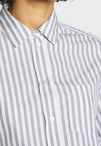 Gestreept shirt met grijze en witte verticale strepen, een klassieke kraag, sluiting met knopen aan de voorkant en een borstzak. Glad stoftextuur.