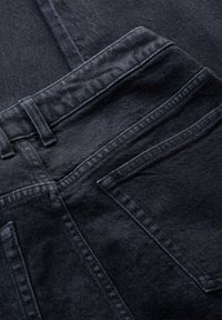 Černé denimové džíny s pevným pasem, několika zadními kapsami a jemnou texturou s tmavými švy.