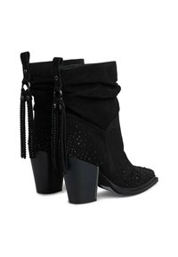 Botas de tobillo de ante negro con un diseño arrugado, detalles de tachuelas y acentos de flecos. Cuenta con tacones gruesos y estables.