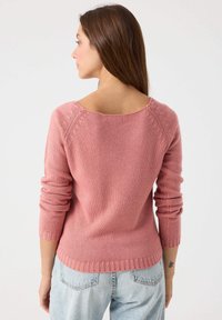 Suéter de punto rosa con un escote amplio en la espalda, puños y dobladillo acanalados, y una textura suave, combinado con jeans azul claro.
