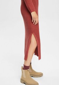 Robe tricotée de couleur rouille avec manches longues, fente latérale et texture côtelée, associée à des bottines beiges et des chaussettes bordeaux.