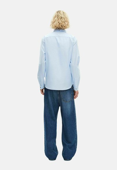 Camisa de manga larga azul claro con cuello clásico, combinada con unos vaqueros de denim azul oscuro de corte holgado. Presenta puños con botones y una pieza en la espalda.
