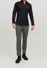 Svart skjorta med knappar och krage, i kombination med texturerade grå byxor och svarta ankelboots. Fokus på tyg och ren design.