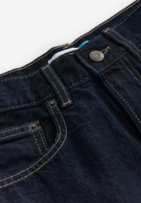 Donkerdenim jeans met een strakke uitstraling, voorzien van contrasterende gele stiksels, een metalen knoopsluiting en een zakdetail.