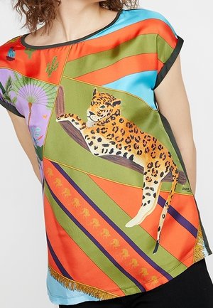 Vrouw draagt een kleurrijk T-shirt met diagonale strepen en een gedetailleerde illustratie van een luipaard die op een tak ligt.