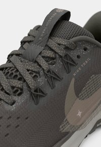 Nike Pegasus Trail 5 jalanijalu tumed tume hallhall, millel on tekstureeritud ülemine osa, võrgulise ja lipsukujundusega, allkiri logo ning heledate aktsentidega hall tald.