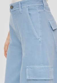 Helle blaue Cargo-Hosen mit glatter Textur, Seitentaschen und kontrastierenden Nähten. Sie verfügen über einen Knopfverschluss und Gürtelschlaufen.