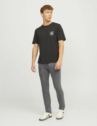 Černé bavlněné tričko s kulatým výstřihem, krátkými rukávy a malým logem na levé straně hrudi. Nosené s šedými slim-fit džíny a teniskami.