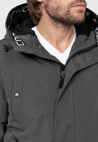 Gray hooded jacket with a zip front, featuring a fleece-lined hood, snap buttons, textured fabric, and logo detailing on the inner collar.